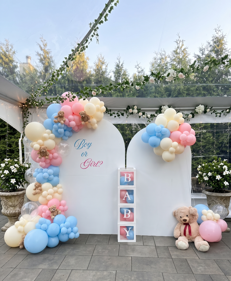 Gender reveal party setup with balloon arches and teddy bears outdoors.